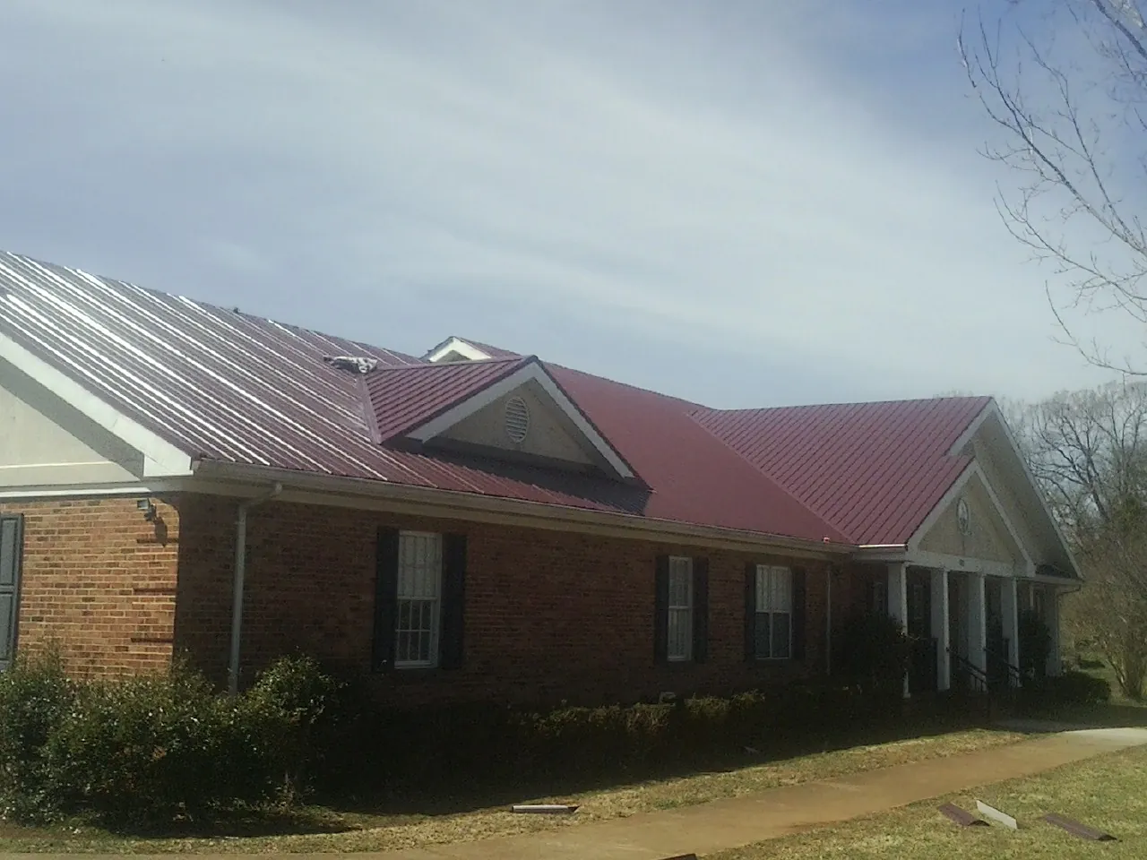 Red metal roof with gabled entries on a long brick building, from a Hail Damage Roof Repair job in North Middletown
