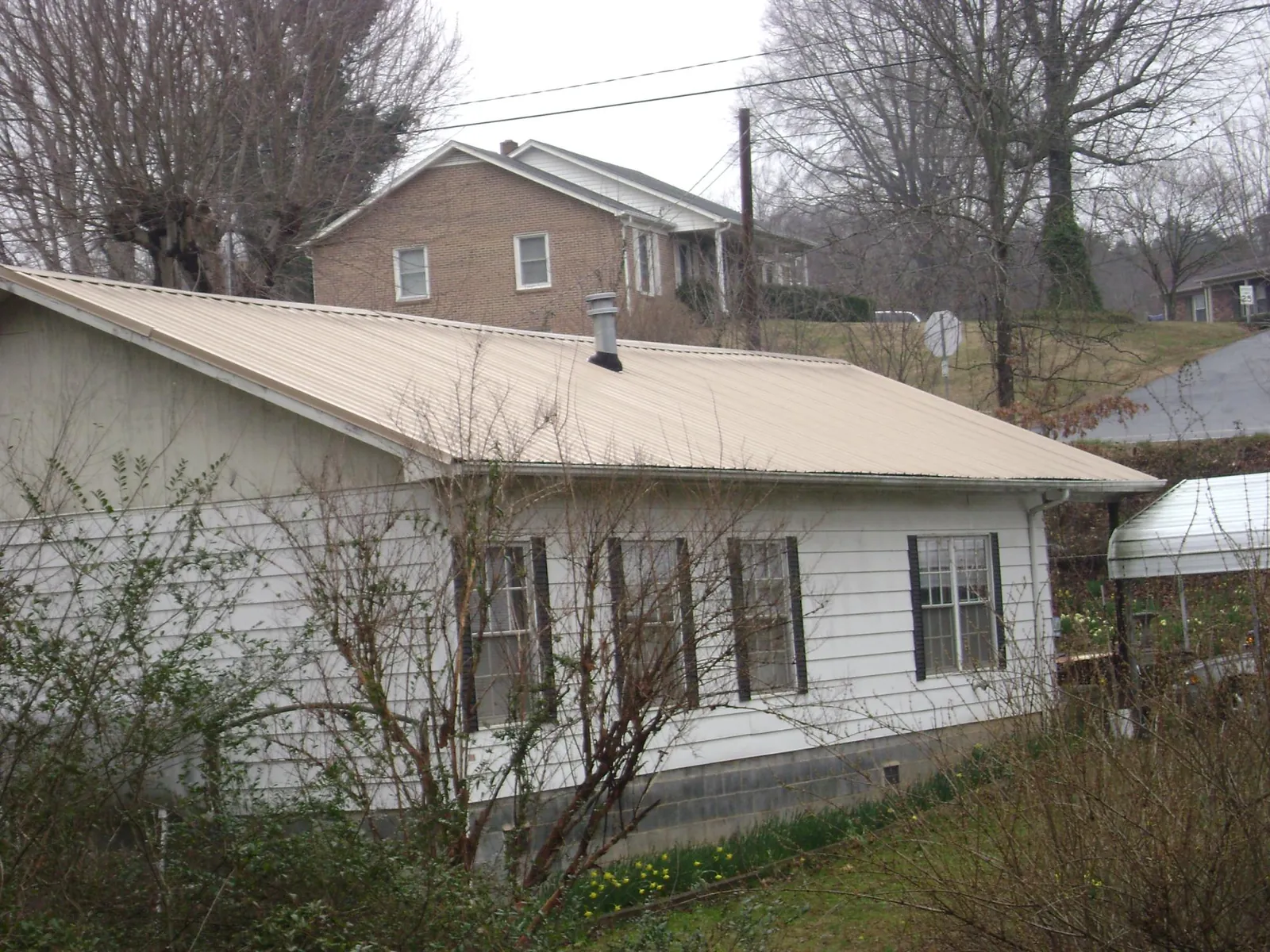 Tan metal roof on a white sided house set into a hillside — Commercial Roofing by Roofing Brothers in North Middletown